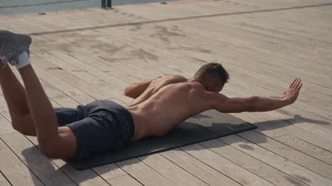 A fit caucasian man does Superman Back Extensions on a black mat. Isometric Stock Footage 218478375