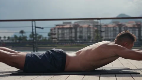 A fit caucasian man does Superman Back Extensions on a black mat. Isometric Stock Footage 218983353