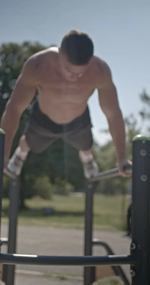 Fit Caucasian Man Doing Dips on Parallel Bars in a Sunny Park: A Vertical Stock Footage 311930162