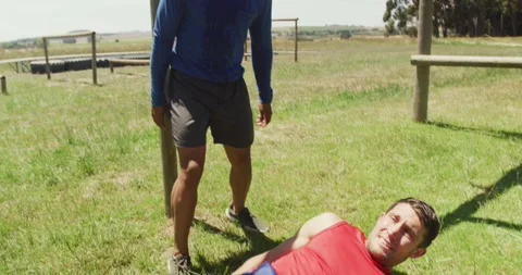 Fit caucasian man falling from bars at obstacle course helped by african Stock Footage 337623296