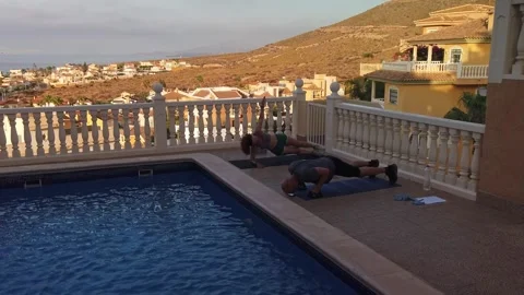 Fit Couple Doing Push Ups and Plank Arm Raises by Villa Pool at Sunset Stock-Footage 345386021