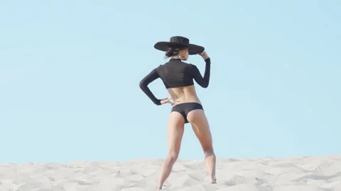 Fit female dancer gracefully performing on sandy dunes under a clear blue sky Stock Footage 311639617