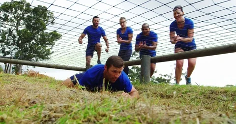 Fit man crawling under the net during obstacle course while fit people cheering Stock Footage 82243157