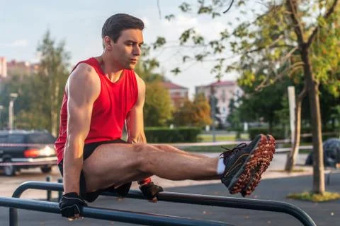 Fit man doing abdominal exercise on parallel bars in summer park Stock-Fotos