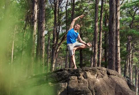 Fit man doing the bending tree pose in a forest Stock Photos