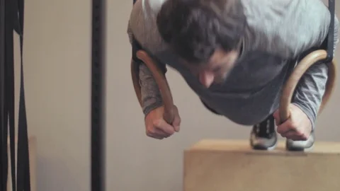 Fit man doing gymnastic ring press ups on a box in the gym Stock Footage 77049562