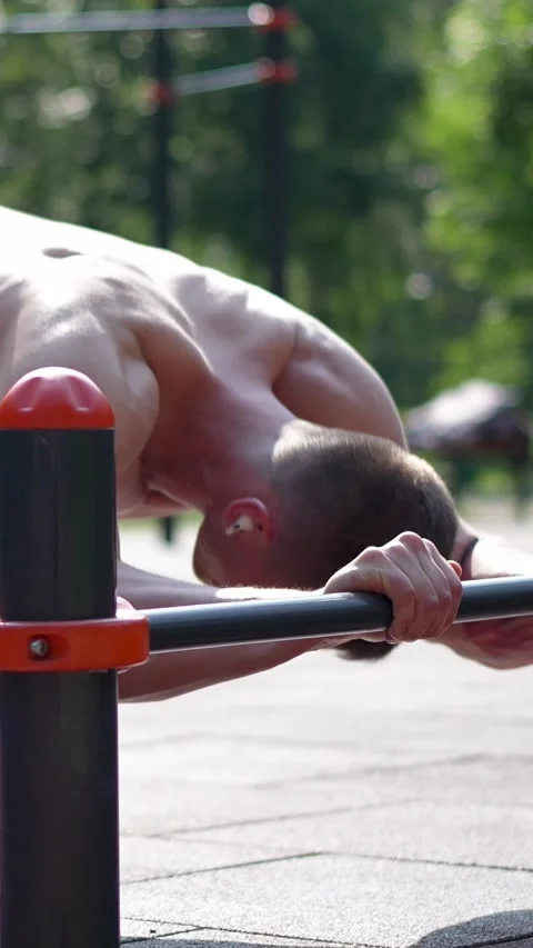 Fit man doing push ups behind the bar outdoors Vertical video Stock Footage 246531605
