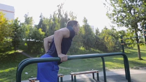 Fit man doing triceps dips on parallel bars at park exercising at sunset Video stock 83676547