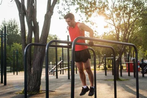 Fit man doing triceps dips on parallel bars at park exercising outdoors Foto stock