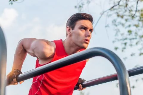 Fit man doing triceps dips on parallel bars at park exercising outdoors Stock Photos