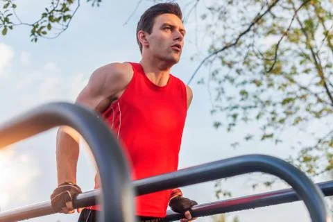 Fit man doing triceps dips on parallel bars at park exercising outdoors Stock Photos