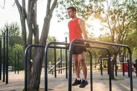 Fit man doing triceps dips on parallel bars at park exercising outdoors 写真素材