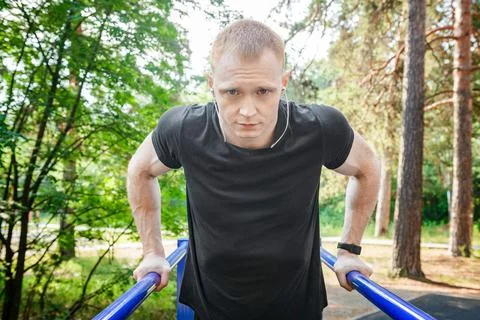 Fit man doing triceps dips on parallel bars at park exercising outdoors. Stock Photos