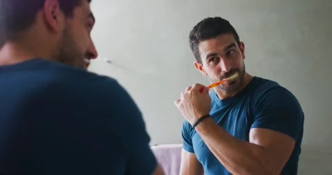 Fit man facing mirror, using orange toothbrush and brushing teeth in bathroom, Stock Footage 340070461