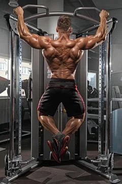 Fit man performs pull ups on cable machine in well equipped gym. He focuses on Stock Photos