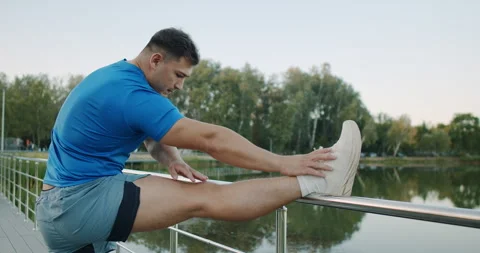 A Fit Man Practicing Stretching Exercises Outdoors by the Tranquil Waterbody Stock Footage 318074059