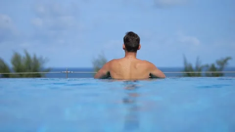 Fit man rises above pool edge gazing at lush tropical landscape Stock Footage 302150823