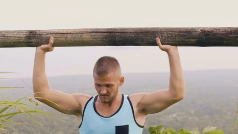 Fit man training press exercise with wooden barbell on natural landscape. Strong Stock Footage 107139453