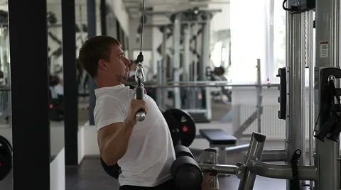 Fit man using the weights machine for his arms at the gym Stock Footage 46019856