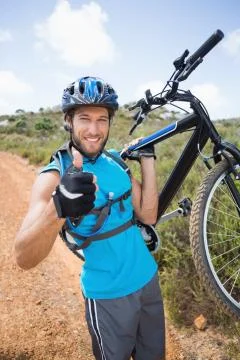 Fit man walking down trail holding mountain bike smiling at camera Stock Photos