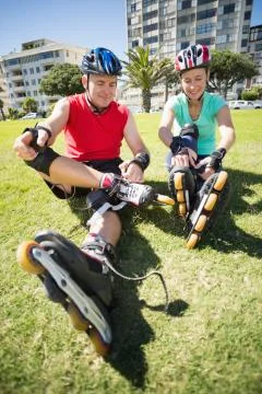 Fit mature couple tying up their roller blades on the grass Stock Photos