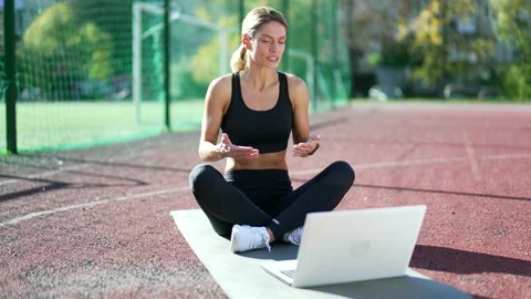 Fit mature female instructor doing online gymnastics training using laptop while Stock Footage 234875466