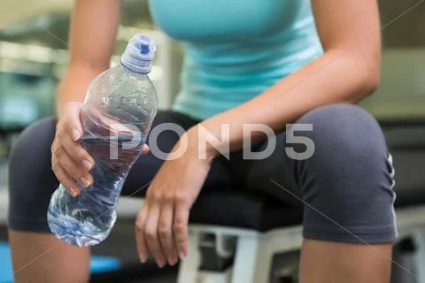 Fit woman sitting on bench holding water bottle Stock Photos