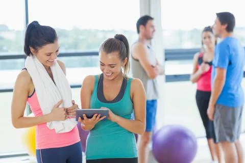Fit women looking at digital table with friends chatting in background Stock Photos