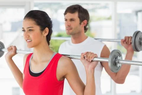 Fit young couple lifting barbells in gym Stock Photos