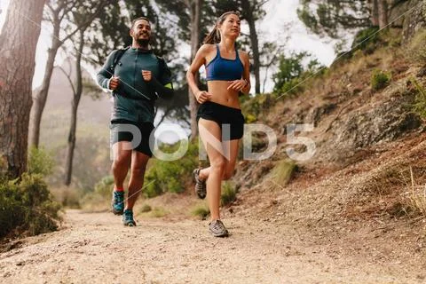 Fit young couple running on mountain trail in morning Stock Photos