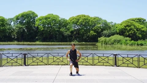 Fit young man doing lunges by the lakeside in a city park. Video stock 300104646