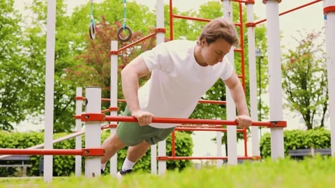 Fit young man doing push-ups on a bar at an outdoor gym. Healthy active lifestyl Stock Footage 337088138