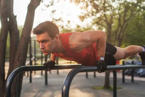 Fit young man doing push ups on horizontal bar outdoors Stock-Fotos