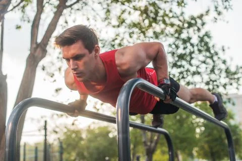 Fit young man doing push ups on horizontal bar outdoors Stock Photos