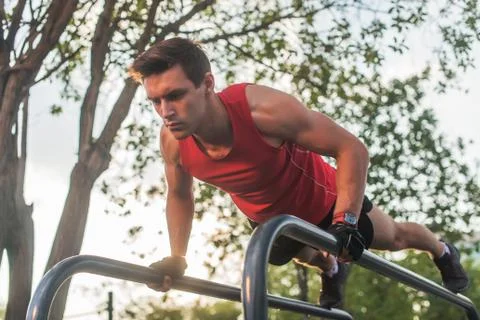 Fit young man doing push ups on horizontal bar outdoors Stock-Fotos