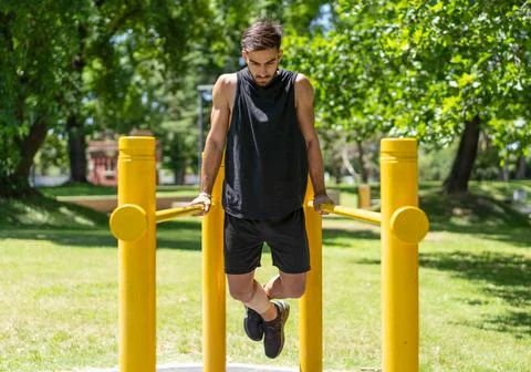Fit young man executing dips on outdoor parallel bars in the park Stock Photos
