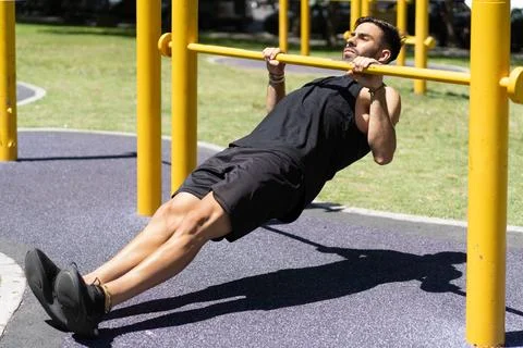 Fit young man executing inverted rows on outdoor gym bars Stock Photos