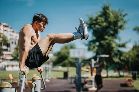 Fit young man exercising on parallel bars in outdoor gym on a sunny day Stock Photos