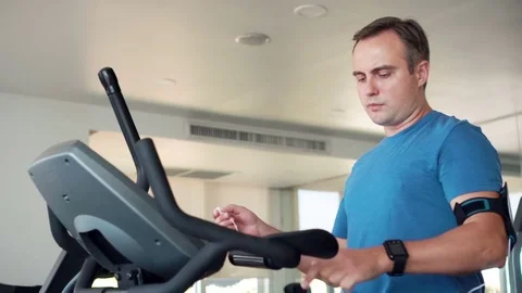 Fit young man in gym doing exercises on velosimulator. Listening music on Stock Footage 76473253