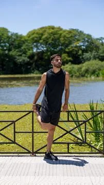 Fit young man performs quadriceps stretches next to a tranquil lake in an u.. Stock Photos