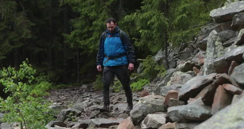 A fit young man is walking alone on a rocky terrain, coming out of the forest. Stock Footage 243750785