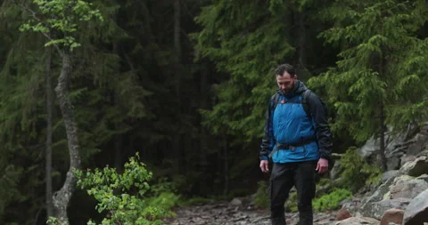 A fit young man is walking alone on a rocky terrain, coming out of the forest. Stock Footage 243751313