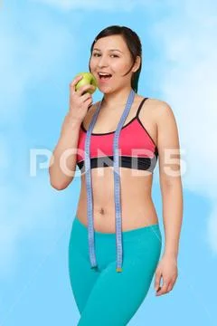 Fitness girl with centimeter and Apple in hand on blue sky background Stock Photos