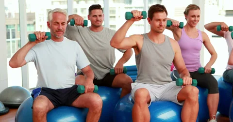 Fitness group sitting on exercise balls lifting hand weights Video stock 34261894