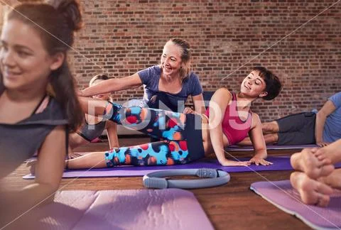 Fitness instructor adjusting young woman in exercise class gym studio Stock Photos