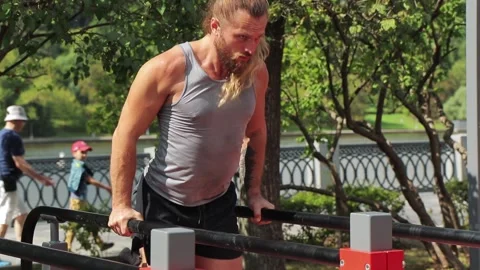 Fitness instructor do dips on the dip bars, people walking in the background Stock Footage 140137607