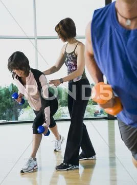 Fitness instructor helping woman lunge with dumbbells Stock Photos
