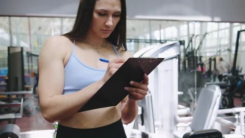 Fitness trainer documenting workout plan in modern gym during afternoon session Stock Footage 318034266