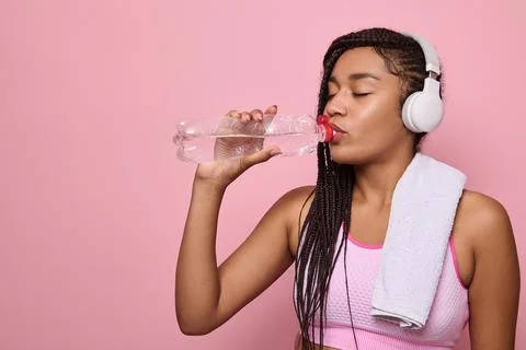 Fitness woman drinking water standing on pink background with copy space. Por Stock Photos