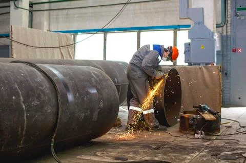 Fitter processes pipe edge with electric hand grinder Stock Photos